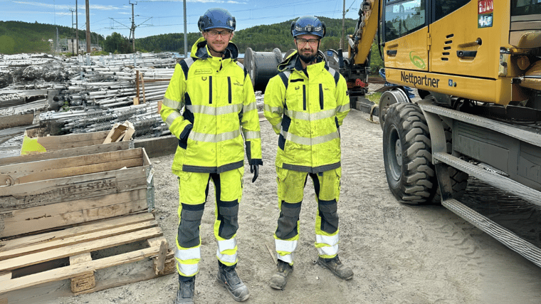 To ansatte i verneutstyr foran Nettpartner-maskin og materialer på byggeplass under åpen himmel.
